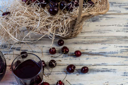 Cherry and cherry juice or wine on a wooden table, a decanter and a glass with juice, a basket with...