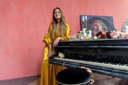 young beautiful woman near the piano in a gold dressの写真素材