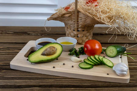 Tomatoes, cucumbers and avocado on the table and in a basket, olive oil and balsamic vinegar,...