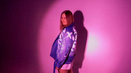 Young beautiful woman with long hair and green eyes. dressed in a stylish leather jacket, shot in pink neon lightの写真素材