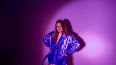 Young beautiful woman with long hair and green eyes. dressed in a stylish leather jacket, shot in pink neon lightの写真素材