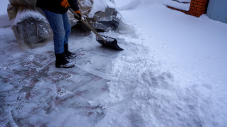 A man cleans snow in the winter in the courtyard of the house. A man cleans the snow with a shovel.の写真素材