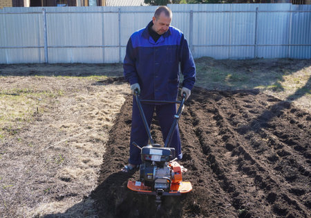A man works in a vegetable garden in early spring. Digs the ground. Works as a cultivator, walk-behind tractor.の写真素材