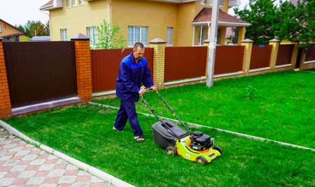 The man is working in the garden. Mowing grass with a lawn mower.