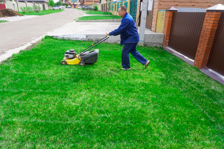 The man is working in the garden. Mowing grass with a lawn mower.