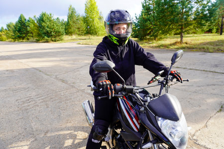 woman motorcyclist in a helmet, motorcycle gloves, motorcycle boots on a motorcycle close-upの写真素材