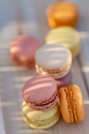 Delicious sweet airy French pastries on a rustic table. Dessert macarons in the summer evening in the orchard. Sunlight. Blurry background. Soft focus. Closeup. Copy space.の写真素材