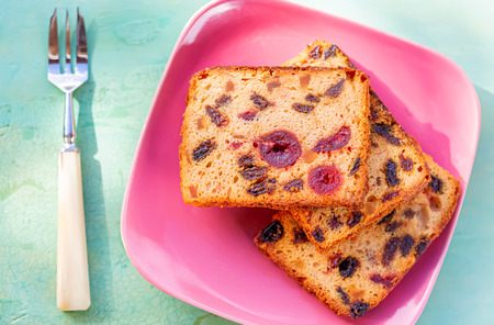 Pastries. A cake slice with fruits on a pink plate. Fruit cake raisin and cherry. Berry muffins on a rustic wooden table. Soft focus. Blurry background. Copy space. Macro and top view.の写真素材