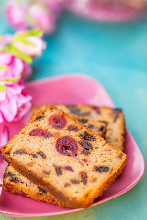 Pastries. A cake slice with fruits on a pink plate. Fruit cake raisin and cherry. Berry muffins on a rustic wooden table. Soft focus. Blurry background. Copy space. Macro and top view.の写真素材