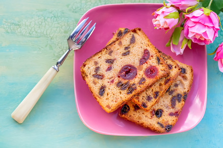 Pastries. A cake slice with fruits on a pink plate. Fruit cake raisin and cherry. Berry muffins on a rustic wooden table. Soft focus. Blurry background. Copy space. Macro and top view.の写真素材