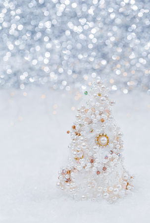 Glamorous white artificial Christmas tree made of pearls and beads on the snow next to a beautiful blurred bokeh background and glowing garland.  Shallow depth of field.Toned image. Copy space.Closeupの写真素材