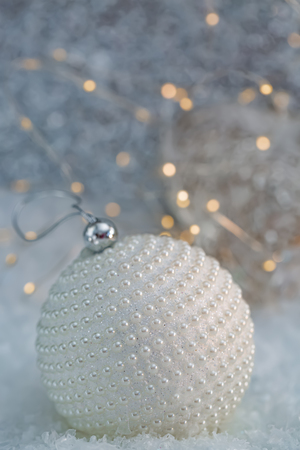 Holiday decoration.White ball with nacre pearls on a snow and beautiful blurred background of glittering bokeh with glowing lights. Greeting card. Happy Merry Christmas and New year.Art photographyの写真素材