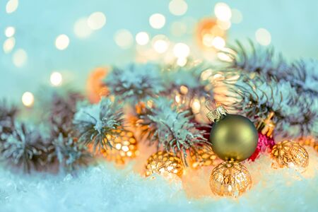 Christmas and New Year Holiday greeting card. Beautiful green ball, pine branches and a garland in the snow. Shallow depth of field. Toned image. Copy space. Blurred bokeh background.の写真素材