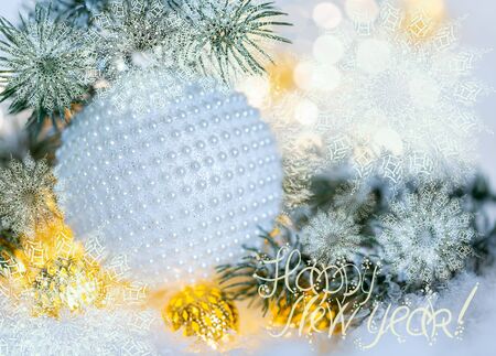 White ball with nacre pearls, pine branches and a garland in the snow. New Year Holiday greeting card. Snowflakes. Text. Shallow depth of field. Toned image. Copy space. Blurred bokeh background.の写真素材