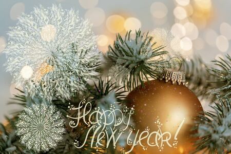 Happy New Year Holiday greeting postcard. Beautiful golden ball, pine branches and a garland in the snow. Snowflakes. Blurred yellow bokeh background. Shallow depth of field. Toned image.の写真素材