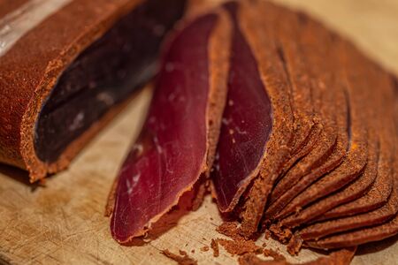 Basturma Beef jerky. Dried meat beef or meat smoked jerky with spices on a wooden cutting board. Armenian food. Shallow depth of field. Closeup. Soft focusの写真素材