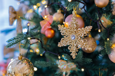 Golden snowflake on a branch of a Christmas tree. Shiny blurry balls. Background with bokeh and glowing garland. Closeup.の写真素材