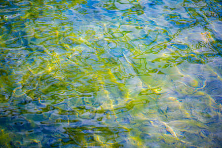 Background with blue, green transparent water surface and waves. Shallow depth of field. Top view.