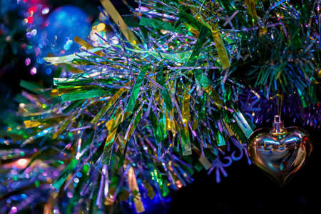 Sparkling heart on a branch of a Christmas tree. Happy New Year, dark postcard. Shallow depth of...