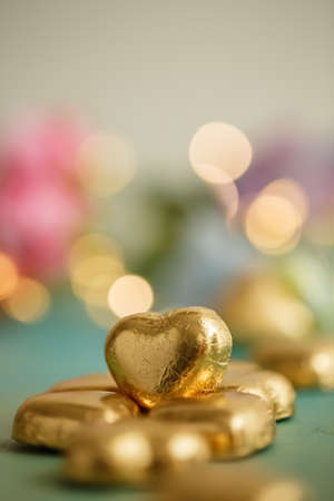Heart shaped chocolates in golden foil on an old table surface. Dark blurred background with bokeh. Wedding greeting glamor card.の写真素材