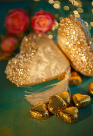 Heart shaped chocolates in golden foil on an old table. Dark blurred background with bokeh. Flowers. Wedding greeting glamor card.の写真素材