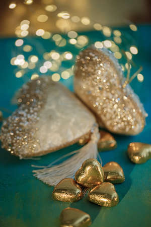 Chocolate candies in the form of hearts in gold foil. Blurred white hearts with bokeh on a green table. Wedding greeting card.の写真素材