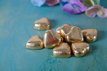 Heart shaped chocolates in golden foil on an old green table. Blurred background with flowers. Wedding card. Soft focus.の写真素材