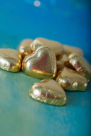 Heart shaped chocolates in golden foil on an old blue, green table. Blurred background with bokeh. Wedding greeting glamor card.の写真素材