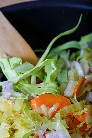 Delicious healthy food. Top view of carrots fried with green cabbage, herbs and onions and a wooden spoon. Vegetarian food.の写真素材
