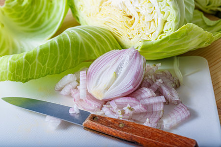 Sliced fresh raw white cabbage, onion on a white plastic board and a small knife. Chopped vegetables. Shallow depth of field.の写真素材