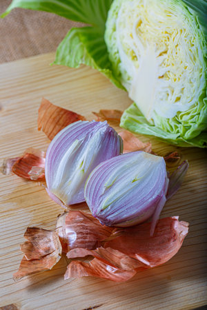 Purple onion with peel and white cabbage on a wooden board. Fresh raw vegetables cut into two parts. Soft focus.の写真素材