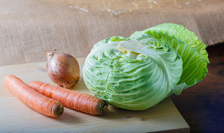 Raw vegetables a cabbage with green leaves, carrots, an onion on a wooden board. A burlap cloth. Vegetarian healthy food.の写真素材