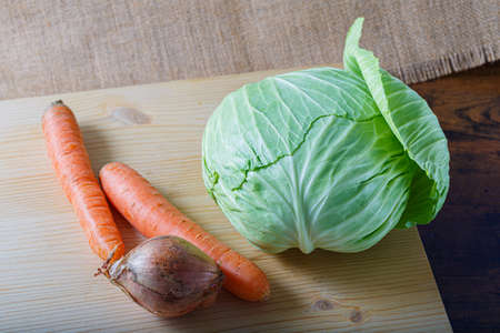 Vegetables carrots, an onion with peel and white cabbage with green leaves on a wooden board. Vegetarian healthy food.の写真素材