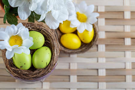 Easter green, yellow eggs with spots and chamomile flowers in a small basket on a wicker surface. Greeting cards for Easter.の写真素材