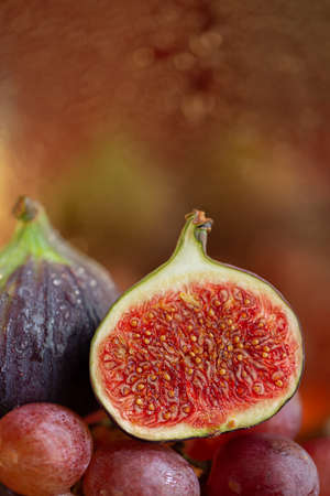 A fig cut in half on pink grapes. Autumn composition of fruits and beautiful bokeh on a blurred background. Shallow depth of fieldの写真素材