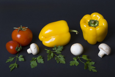 Yellow pepper with mushrooms and tomatoes on a dark background. Composition of mushrooms with tomatoes and yellow pepper on a black background.の写真素材