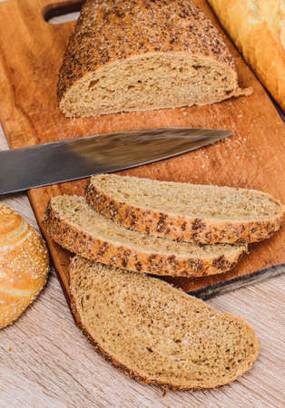 Different breeds on wooden background. Knife on a wooden board with bread and different buns on the...