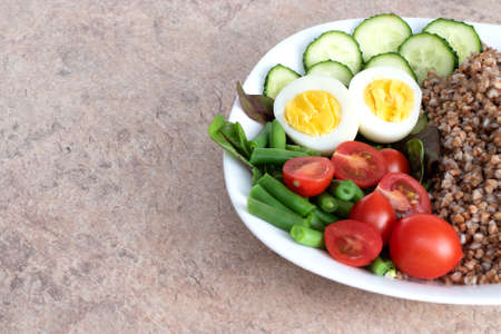 Tasty and healthy food from natural products. Salad of green vegetables, tomato and buckwheat in a white plate. Buckwheat with vegetables and eggs on a white plate.の写真素材