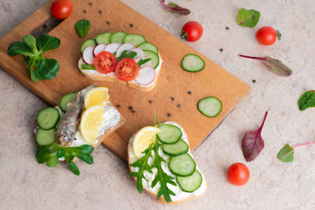 A set of sandwiches with sprats, homemade curd cream with herbs, with radishes, cucumbers, and tomatoes, on a wooden background. Top view. Copy space.の写真素材