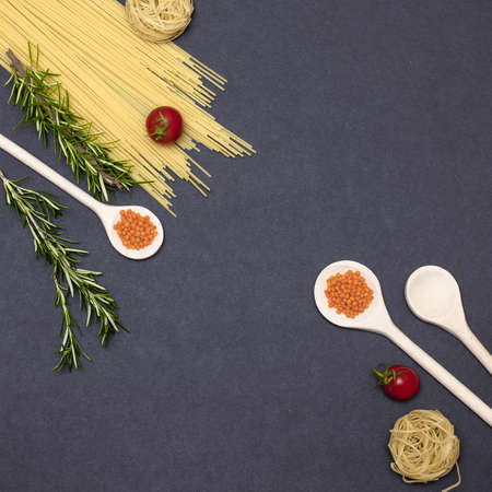 Italian food ingredients.Still life of cooking pasta on a black background top view. Wooden spoons with spices. Frame of products and vegetables.の写真素材