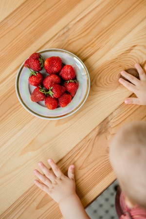 Hand of a child with a strawberry on a rustic background, a plate of strawberries. The concept of summer healthy eating. View from above, apartment.の写真素材
