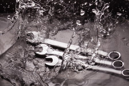 Wrenches of different sizes on a dark background in a spray of water.の写真素材
