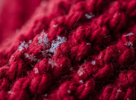 Closeup of a red knitted plaid with few snowflakes on it. Macro shooting.