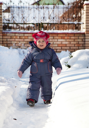 Portrait of a child and a warm winter suit with gloves, playing on a winter day outdoors. Blind snowman, play snowballs child fun.の写真素材