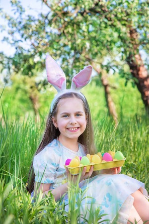 Cute girl with bunny ears on Easter day. A girl is chasing Easter eggs in the garden. The girl has a...