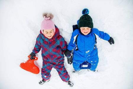 Happy brother and sister lying in the snow. Winter games in the fresh air. Winter vacation.の写真素材