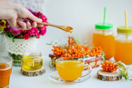 Warm sweet organic tea with sea buckthorn berries, thyme and honey. White background, natural lighting. Horizontal composition with copy space. Concept of beauty in simplicity.の写真素材