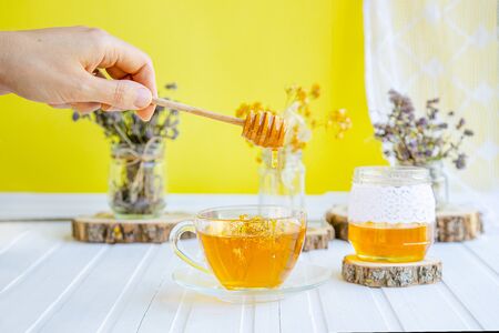 Glass cup of tea with linden in natural organic herbs and a jar of honey on a white wooden table. Increase immunity in the cool season.の写真素材