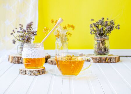 Glass cup of tea with linden in natural organic herbs and a jar of honey on a white wooden table. Increase immunity in the cool season.の写真素材