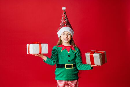 Merry Christmas, happy attractive girl with gifts in a costume of Santa Claus helper elf on a bright...